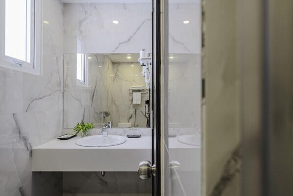 A modern bathroom with marble walls, a glass shower enclosure, and dual sinks. - TTR Moonstone Apart Hotel (Xuan Huong - Da Lat)