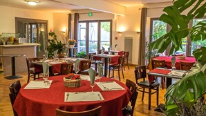 A restaurant with round tables covered in red tablecloths, wooden chairs, and potted plants. - Hotel Les Persedes Sud Ardeche (Lavilledieu)