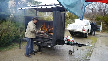 A man grilling outdoors with a portable grill and a truck nearby.