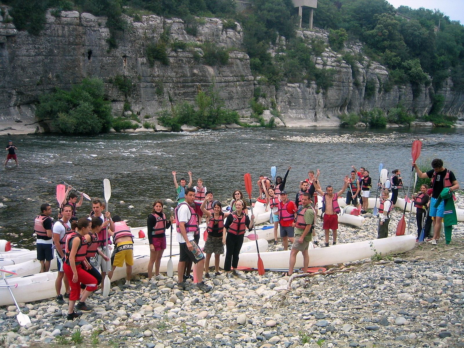 Un groupe de personnes se trouve sur une rive rocheuse, avec des canoës et des kayaks.