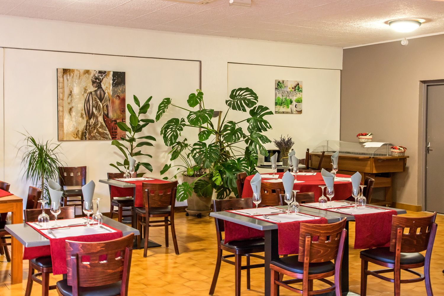 A dining area with tables set for four, surrounded by potted plants and artwork on the walls.