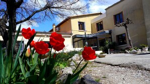 A hotel with a yellow facade, a stone pathway, and red flowers in the foreground. - Hotel Les Persedes Sud Ardeche (Lavilledieu)