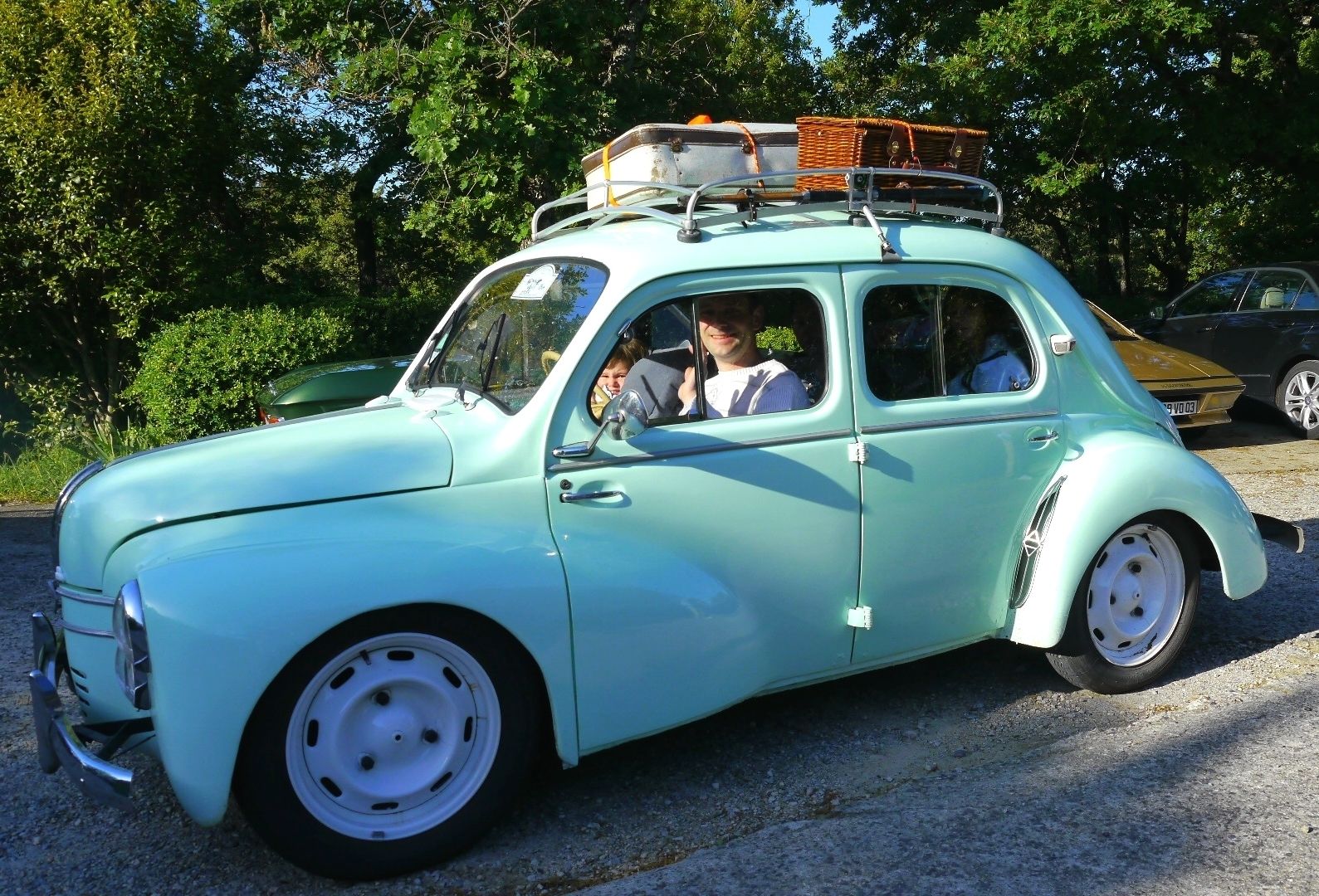 A vintage light blue car with a roof rack and a wicker basket.