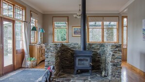 A cozy room with a stone fireplace, wooden flooring, and large windows. - Mataura Lodge | Your Private Rural  Retreat (Athol)