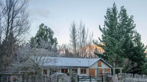 A rustic cabin with a stone wall and wooden fence, surrounded by trees and a clear sky. - Mataura Lodge | Your Private Rural  Retreat (Athol)
