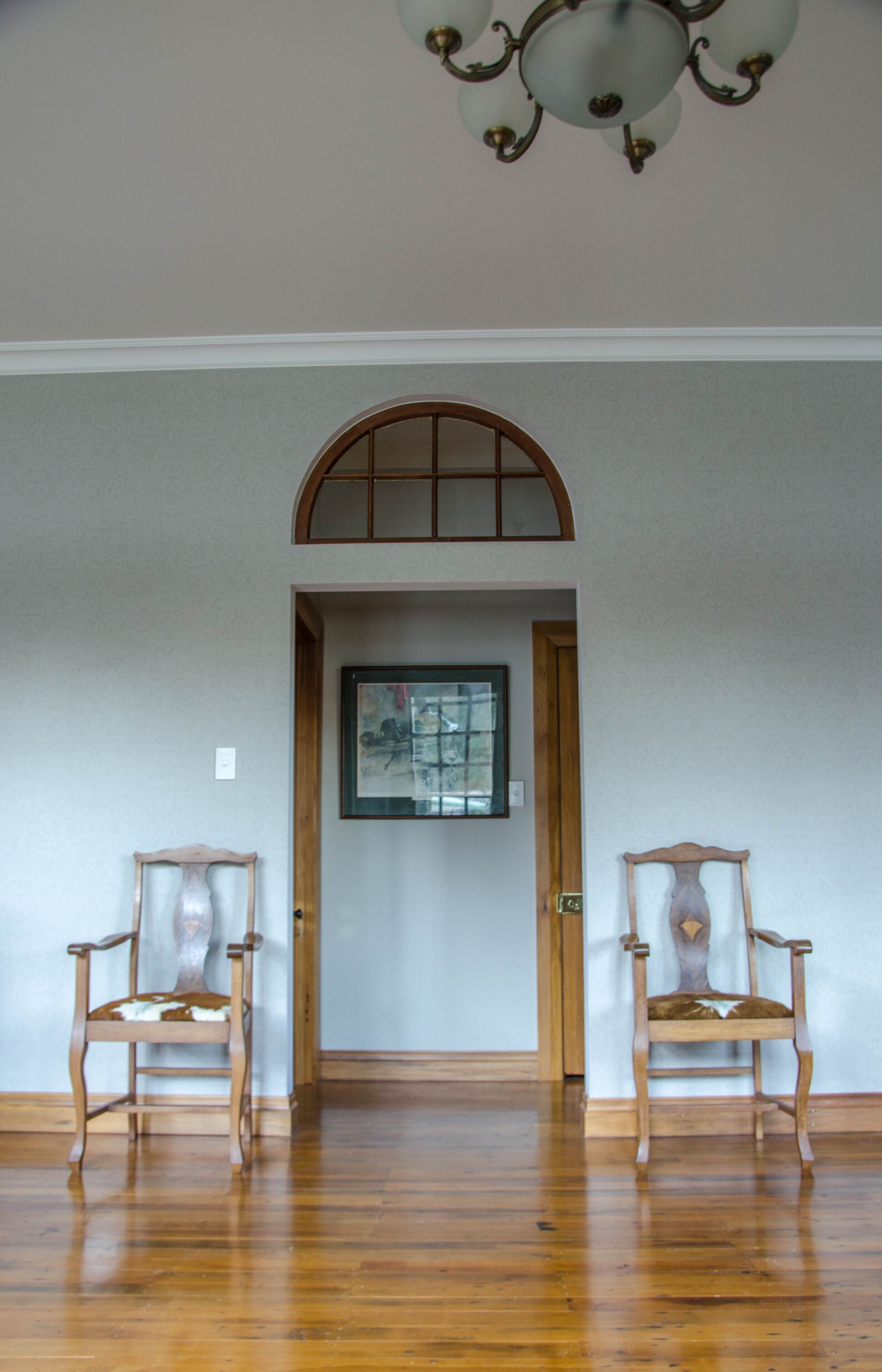 A room with wooden flooring, two chairs, a door with a picture frame, and a ceiling light fixture.