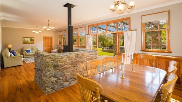 A spacious room with a stone fireplace, wooden dining table, and comfortable seating. - Mataura Lodge | Your Private Rural  Retreat (Athol)
