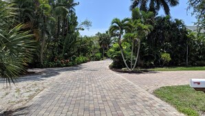 A paved pathway leading through a lush garden with various tropical plants and trees. - Keys stilt house top floor unit (Naples)