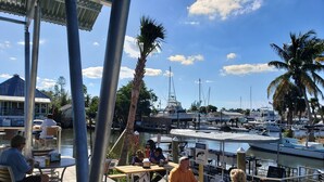 A marina with boats docked, people sitting at tables, and a building in the background. - Keys stilt house top floor unit (Naples)