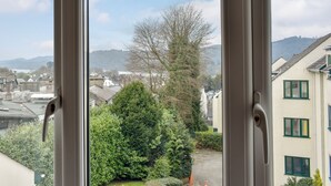 A view through a window of a residential area with buildings, a tree, and hills in the background. - 1 bedroom accommodation in Bowness-on-Windermere (Bowness-on-Windermere)