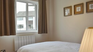 A bedroom with a bed, a window with curtains, a radiator, and framed pictures on the wall. - 1 bedroom accommodation in Bowness-on-Windermere (Bowness-on-Windermere)