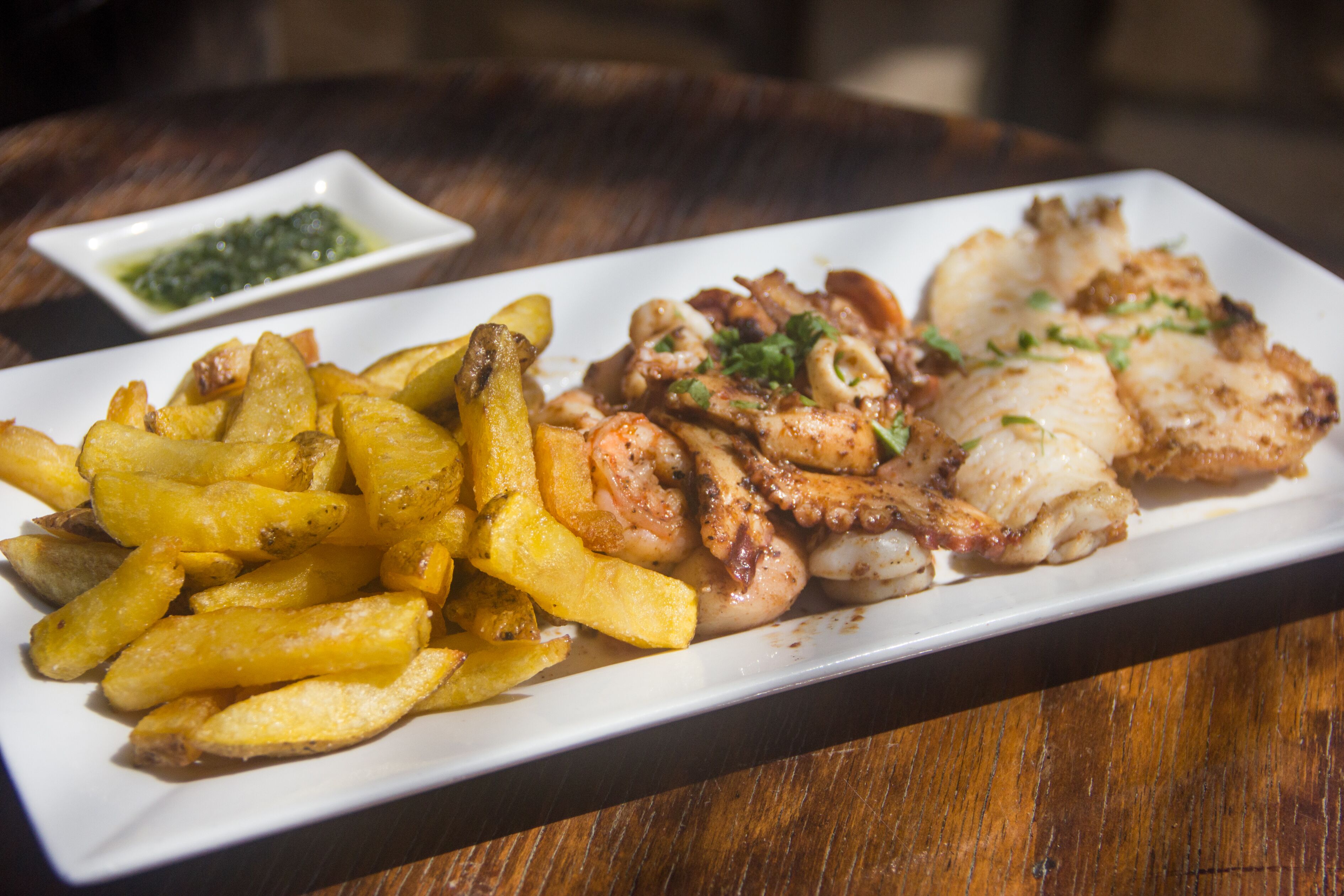 A plate of food with fries and grilled octopus, served on a white rectangular plate.