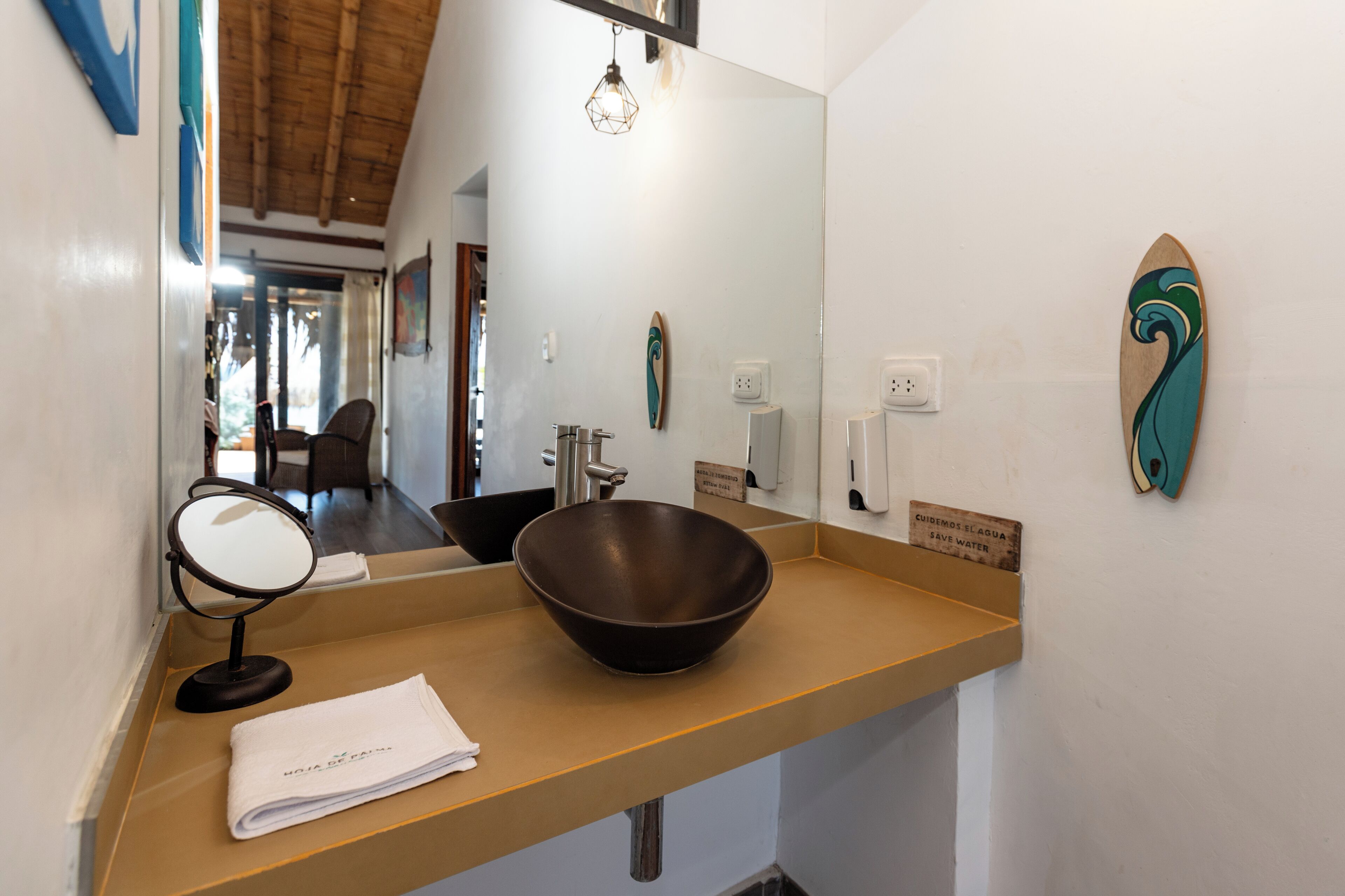 Une salle de bain avec un grand miroir, un lavabo en forme de bol en bois, une serviette et un panneau d’information sur la préservation de l’eau.