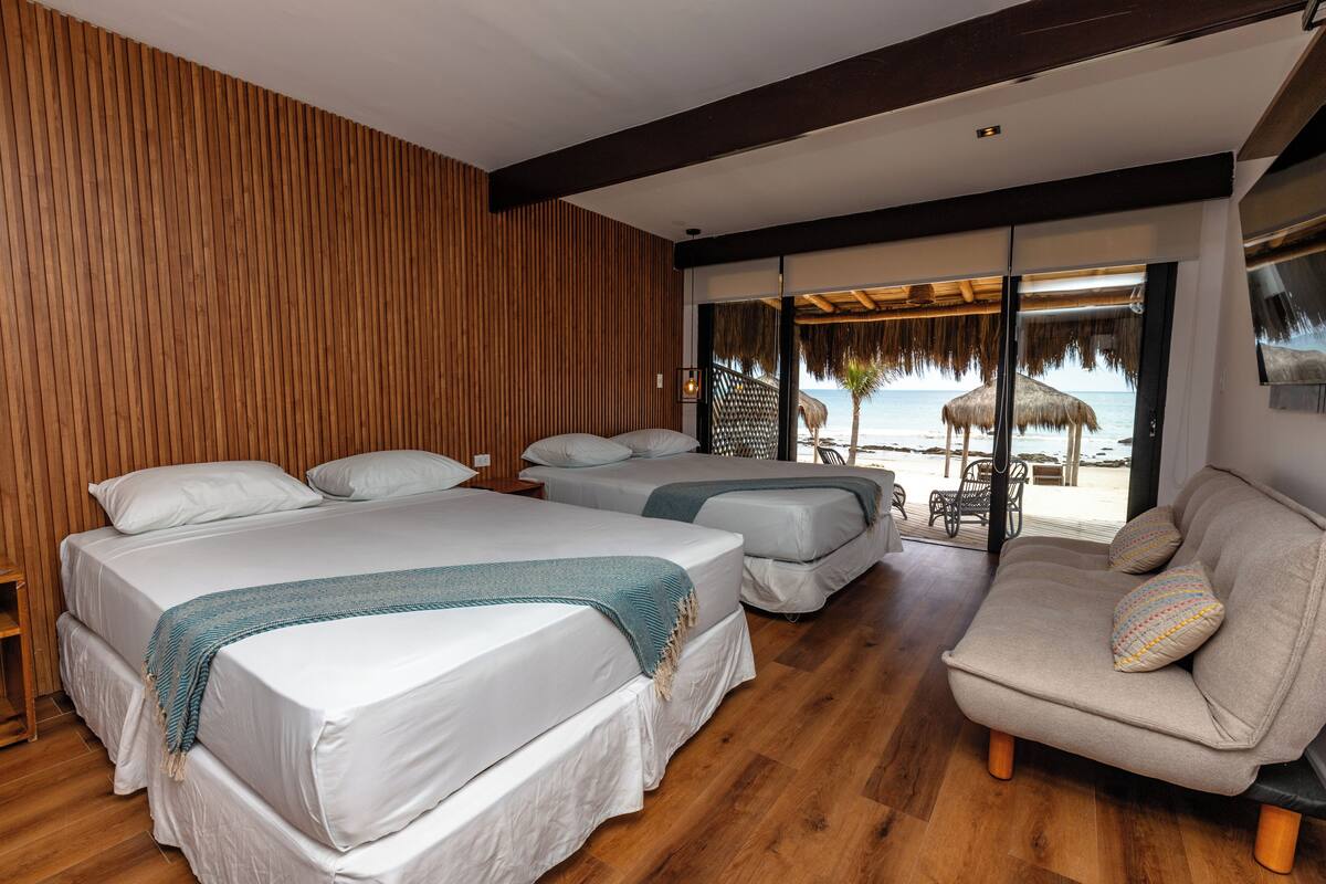 Ein Hotelzimmer mit zwei Betten, einer Schlafcouch, Holzvertäfelung und Blick auf den Strand.