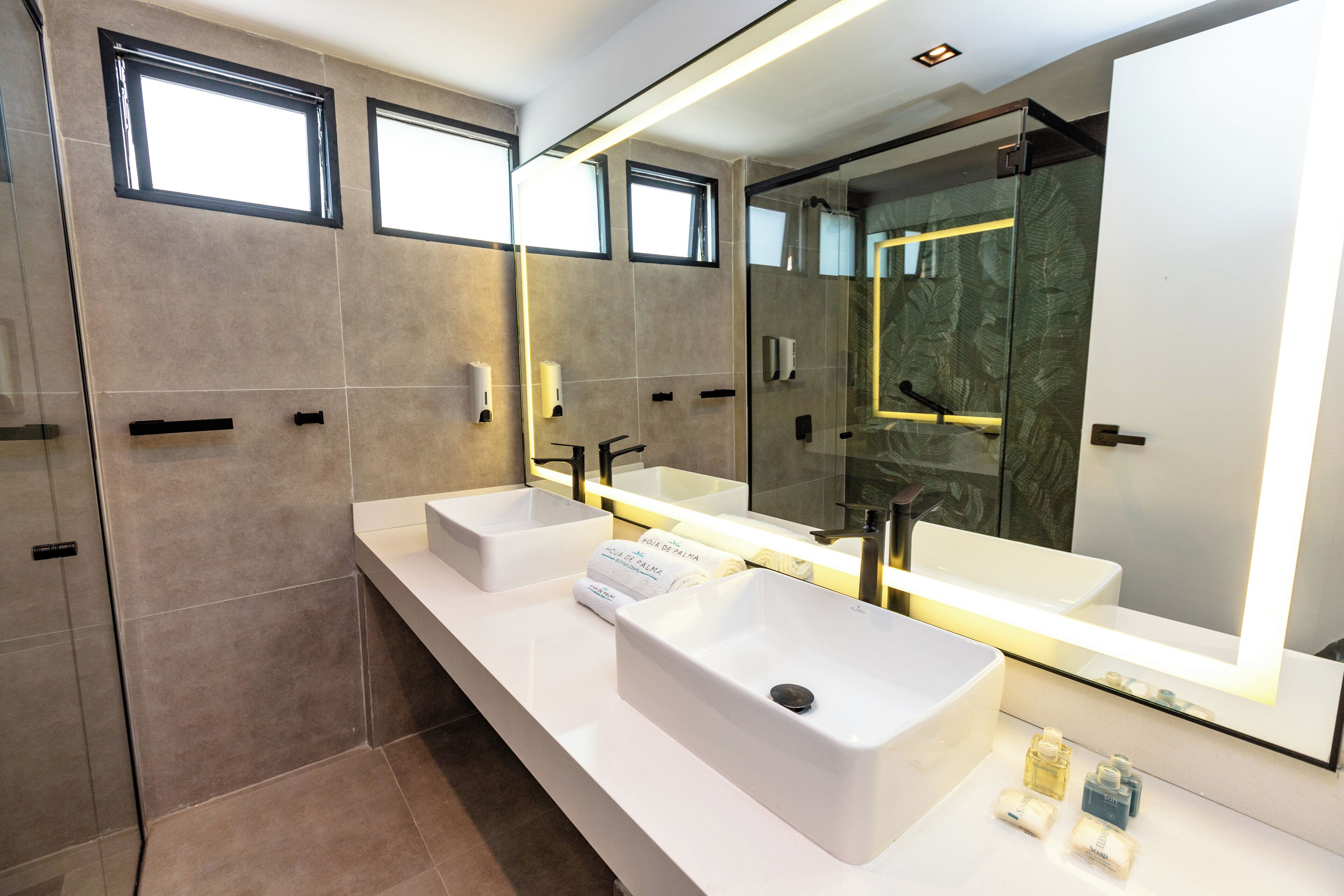 Ein modernes Badezimmer mit zwei Waschbecken, einem großen Spiegel und einer Dusche.