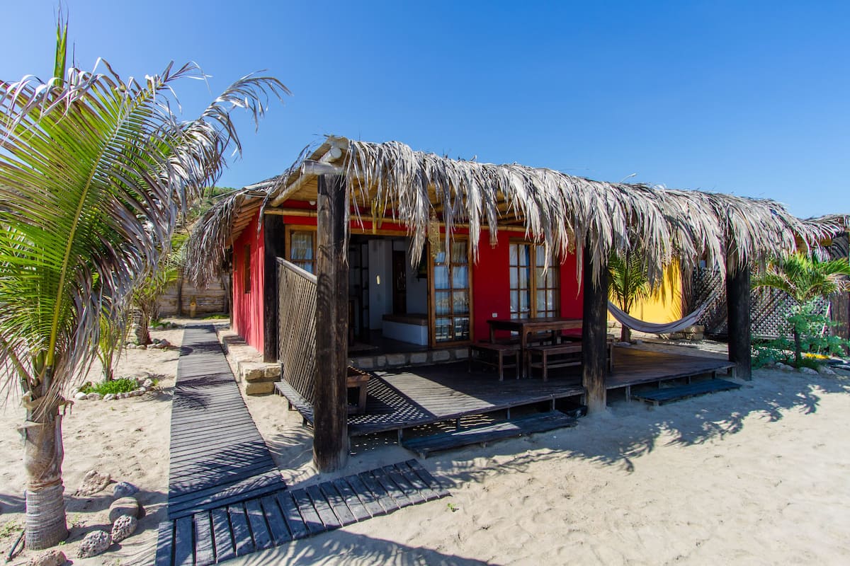 Ein Strandhaus mit einem Reetdach, einer Holzterrasse und einer roten Fassade.