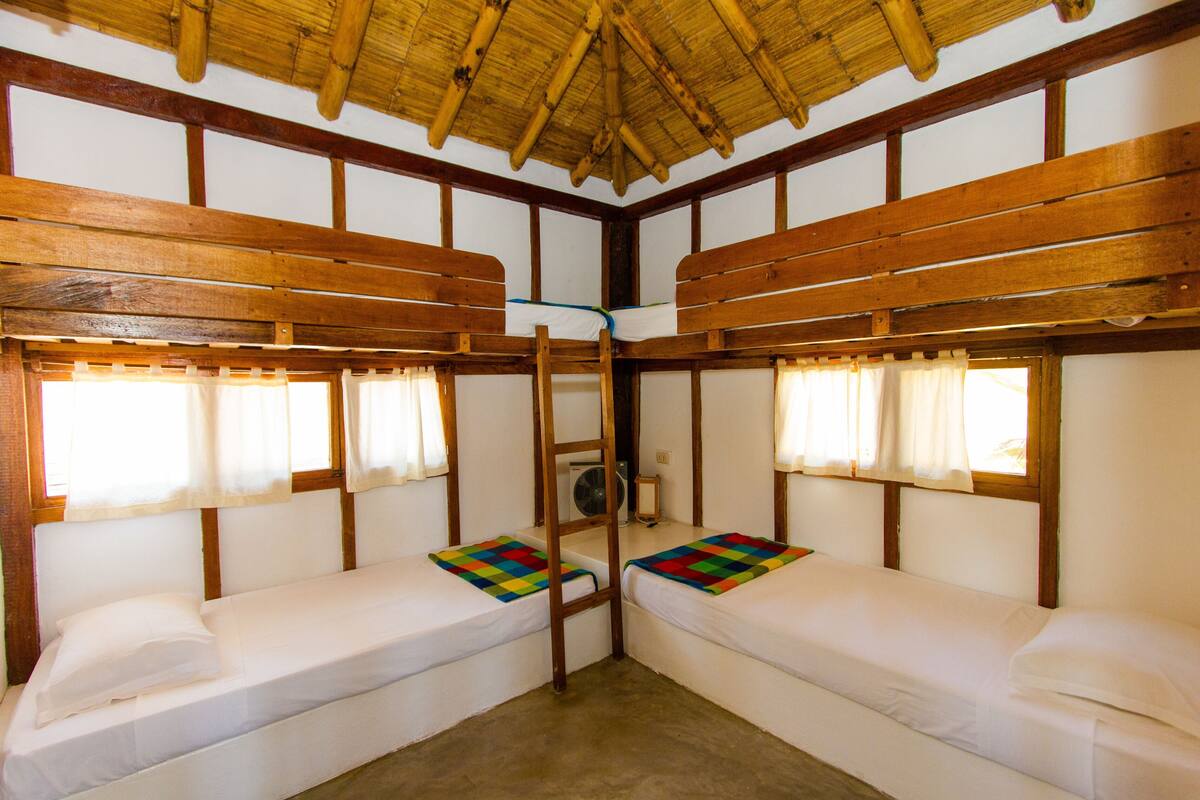 Ein Zimmer mit zwei Etagenbetten, Holzbalken, einem Ventilator und Fenstern mit Vorhängen.