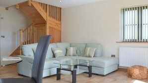 A modern living room with a light-colored sofa, a glass coffee table, and a wooden staircase. - 2 bedroom accommodation in Chard (Chard)