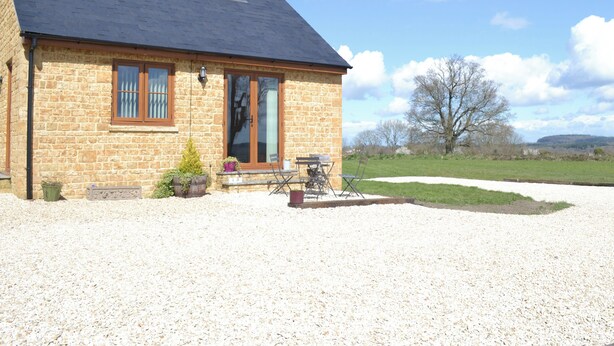 A stone house with a gravel driveway, a wooden door, and a small garden with potted plants. - 2 bedroom accommodation in Chard (Chard)