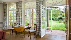 Ein Essbereich mit Holztisch und Stühlen, großen Fenstern mit Vorhängen und Blick auf einen Garten.
