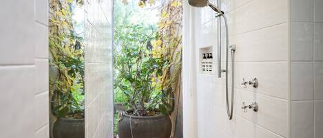 A shower with a glass door, a potted plant, and a tiled wall.
