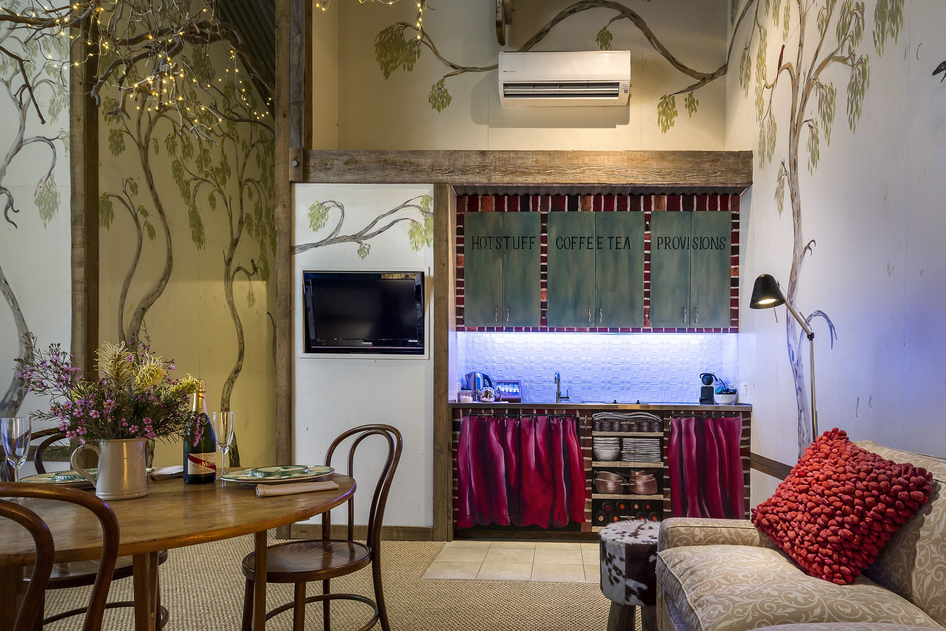 A cozy dining area with a wooden table and chairs, a vase with flowers, and a television on the wall.