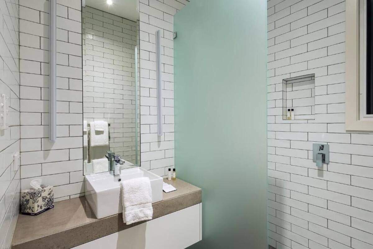 A bathroom with white subway tiles, a beige countertop, a white sink, a mirror, and a green accent wall.