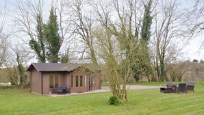 Une petite cabane en bois dotée d’une terrasse, entourée d’un champ verdoyant et d’arbres.