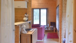 L’intérieur d’un chalet accueillant, avec des murs en bois, un bureau avec un ordinateur, un canapé et une fenêtre équipée de stores.
