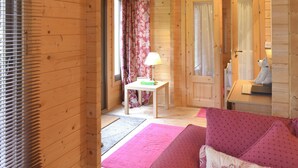 L'intérieur d'un chalet en bois, avec un plancher en bois, un canapé rose, une table blanche avec une lampe et une horloge au mur.