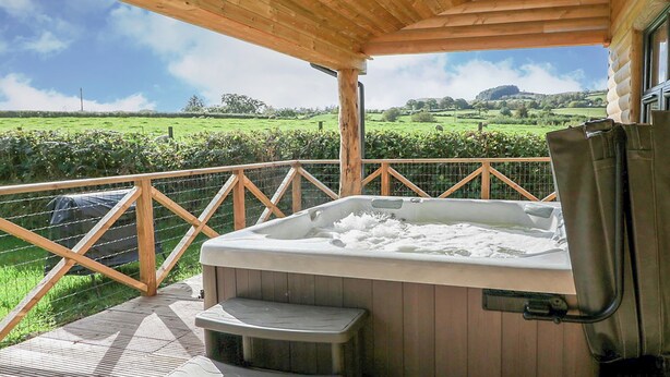 A hot tub on a wooden deck with a view of a green field.