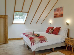 Quarto com claraboia, cama com manta vermelha e branca, mesa de cabeceira com abajur e um quadro na parede.
