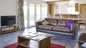 A living room with a leather sofa, a flat-screen TV, a wooden coffee table, and a red rug.
