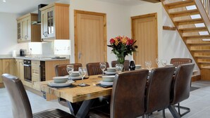 A dining area with a wooden table set for six, surrounded by leather chairs, a chandelier, and wooden doors.