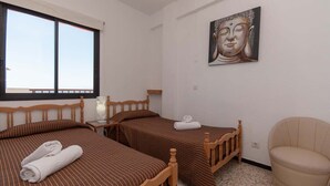 Ein Hotelzimmer mit zwei Einzelbetten, einem Holz-Kopfteil, einem an der Wand befestigten Buddha-Gemälde und einem beigefarbenen Sessel.