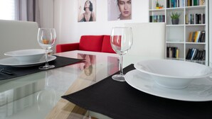 A dining area with a glass table, two wine glasses, and white plates. There is a red sofa and a bookshelf in the background.