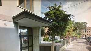 A building with a glass entrance, a small outdoor area with a bench, and a tree in front.