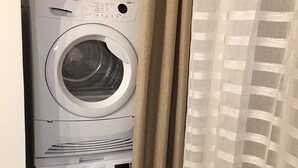 A stacked washer and dryer unit in a laundry room with a striped curtain partially covering the view.