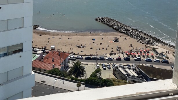 A view of a beach with a rocky breakwater, a sandy shore, and a parking area with cars. - Radar Cabo Corrientes (Mar del Plata)