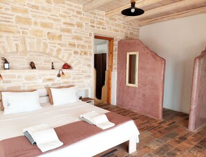 A bedroom with a stone wall, a bed with white bedding, a wooden headboard, and a small mirror on the wall. - Luxury, 2015 stone-built, 2 bedroom Villa with pool and sea view (Καμηλάρι)