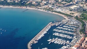 Vue aérienne d’une marina côtière où de nombreux bateaux sont amarrés, entourée de bâtiments résidentiels et d’une plage.