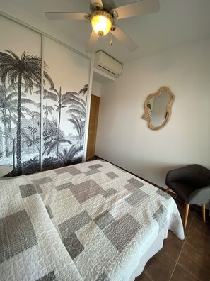 Une chambre à coucher comprenant un lit, un ventilateur de plafond, un appareil de climatisation, un miroir fixé au mur et une chaise.