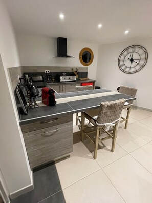 Een moderne keuken met een centraal eiland, twee rieten stoelen, een klok en een rode waterkoker.