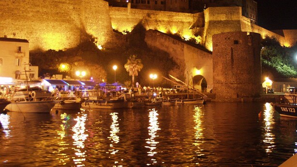 Un site historique situé au bord de l’eau, avec un rempart fortifié, des bateaux amarrés et un bâtiment surmonté d’un dôme.