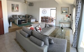 Een moderne woonkamer met een grijze modulaire bank, een eethoek met een houten tafel en stoelen, en uitzicht door een open deur.