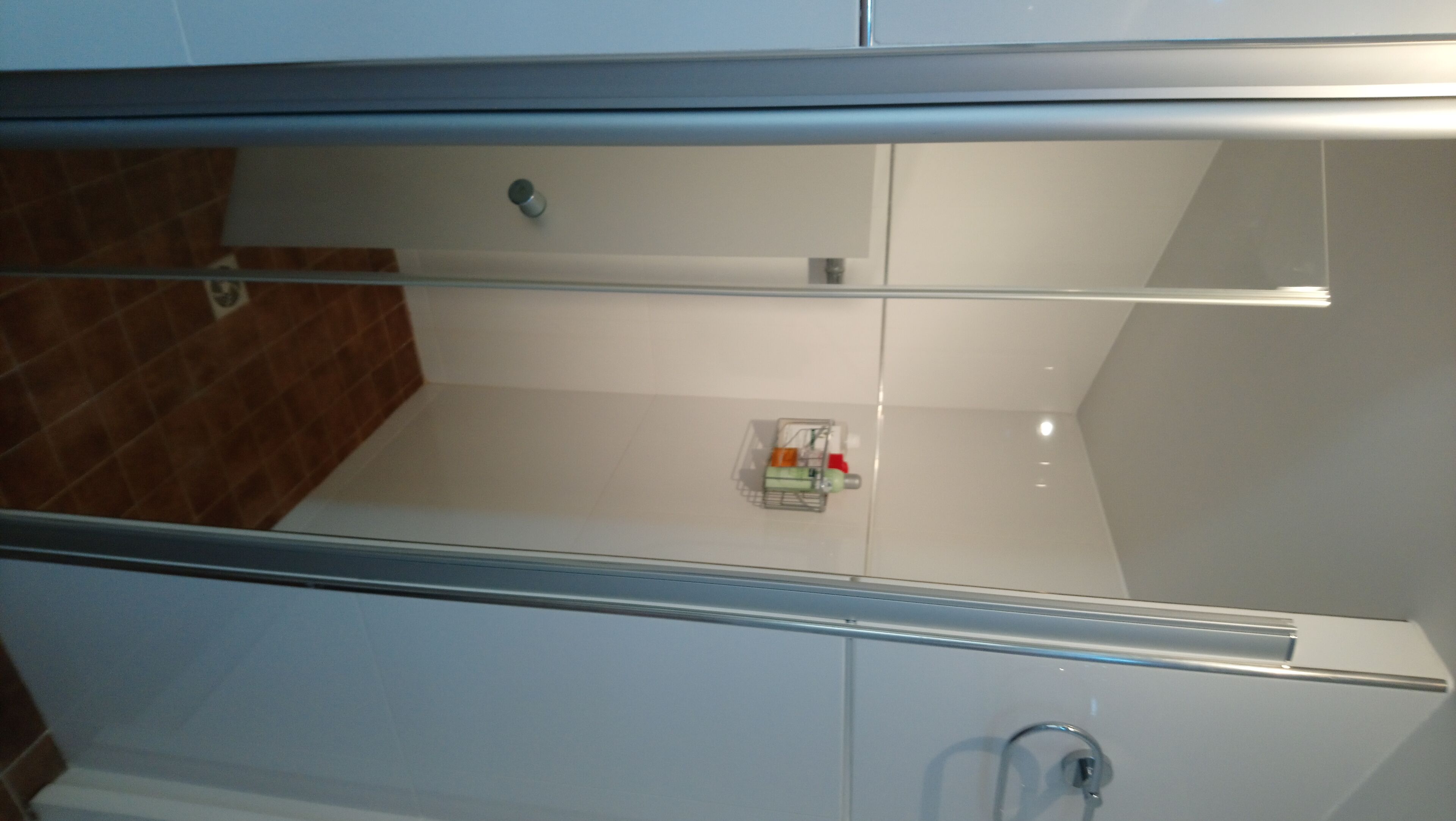 A bathroom with a glass shower enclosure, a white sink, and a small shelf with toiletries.