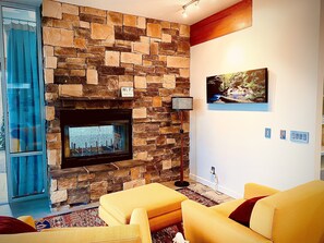 A living room with a stone fireplace, a flat-screen TV mounted above it, and two yellow armchairs.
