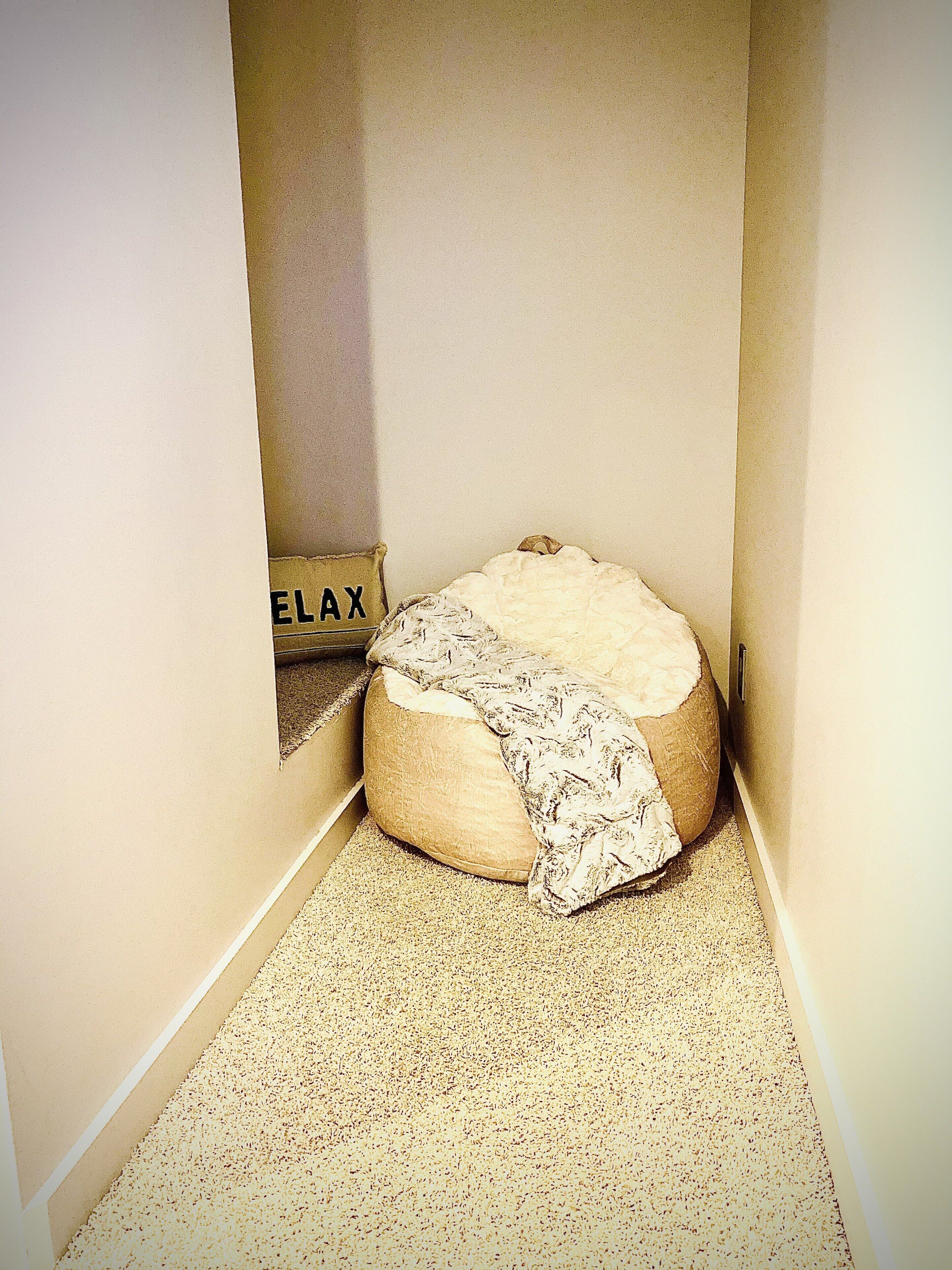 A small, narrow room with a single bean bag chair and a sign on the wall that reads "ELAX".