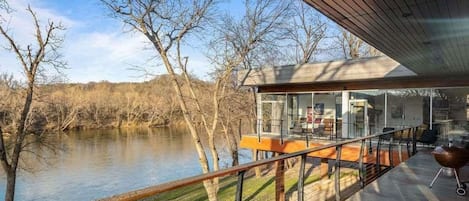 A modern house with a glass conservatory overlooking a river.