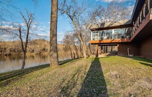 A modern house with a glass conservatory, a view of a river, and a well-maintained lawn.